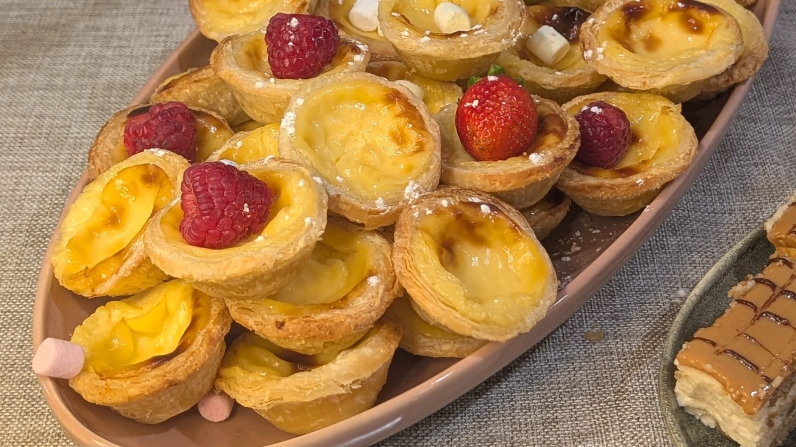 Tabuleiro de pastéis de nata com framboesas sobre toalha de linho